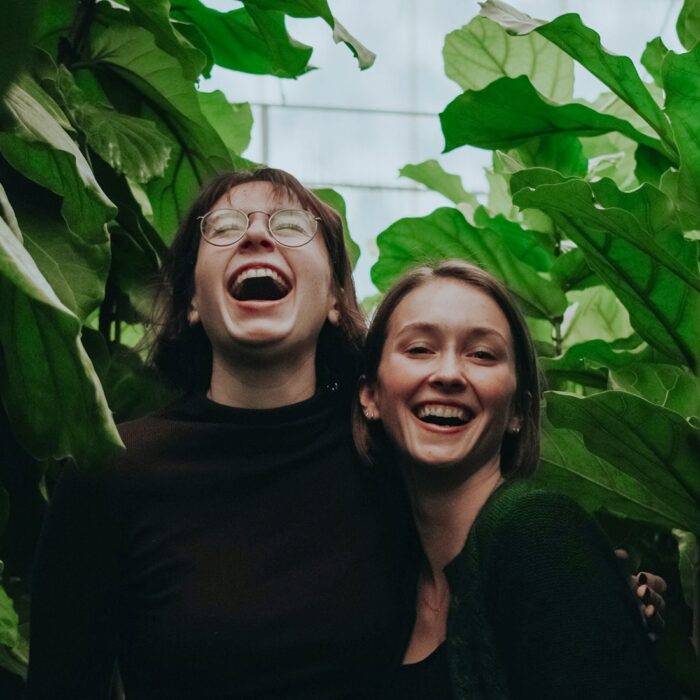 Two people sharing a joyful, laughing moment surrounded by green leaves.